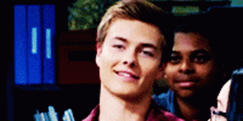 A Young Man In A Red Shirt Is Smiling While Standing Next To Another Man . GIF