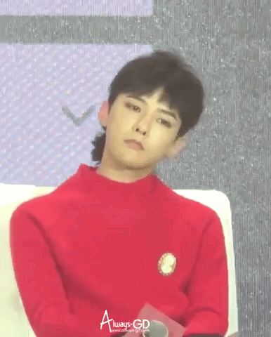 A Young Man In A Red Sweater Is Sitting On A Couch And Looking At The Camera . GIF