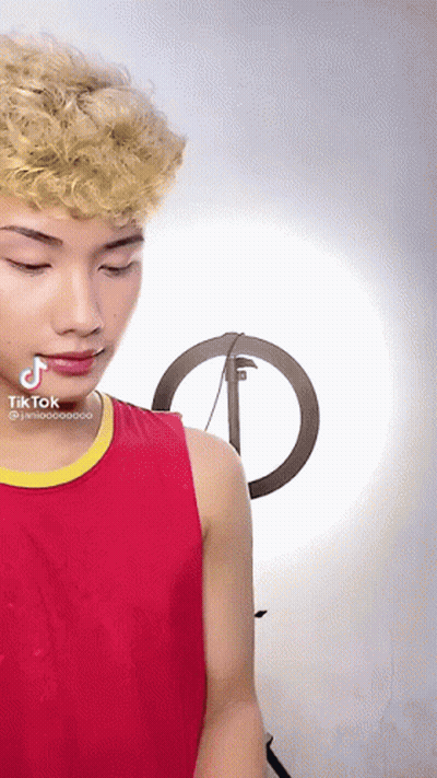 A Young Man In A Red Tank Top With A Yellow Stripe Has A Tik Tok Sticker On His Face GIF