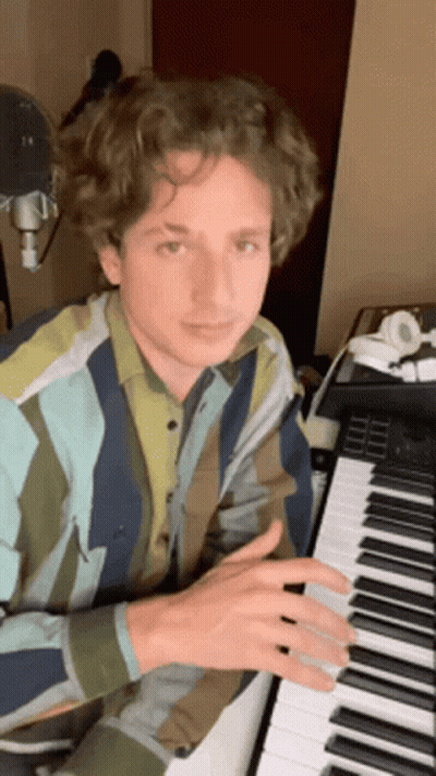 A Young Man In A Striped Shirt Is Playing A Piano In A Room . GIF