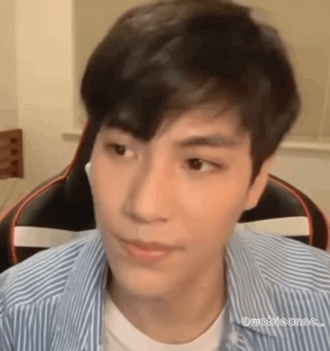 A Young Man In A Striped Shirt Is Sitting In A Chair And Looking At The Camera . GIF