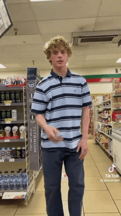 A Young Man In A Striped Shirt Is Standing In A Store GIF