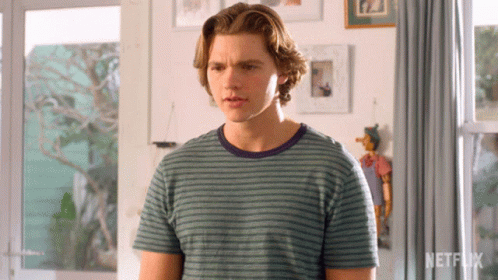 A Young Man In A Striped Shirt Is Standing In Front Of A Netflix Logo GIF