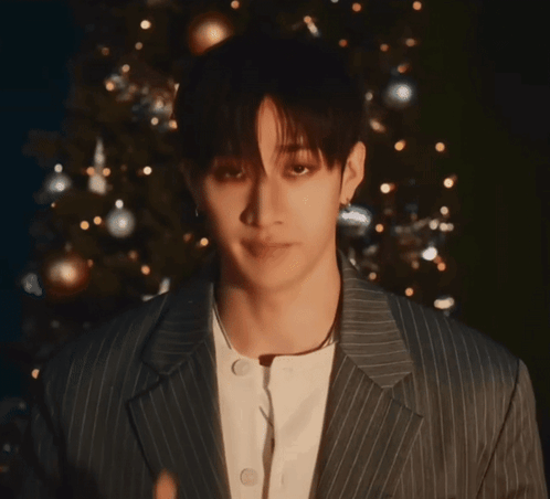 A Young Man In A Striped Suit Giving A Thumbs Up In Front Of A Christmas Tree GIF