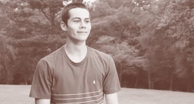 A Young Man In A Striped T-Shirt Is Standing In Front Of A Forest . GIF