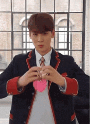 A Young Man In A Suit And Tie Is Holding A Pink Heart In His Hands . GIF