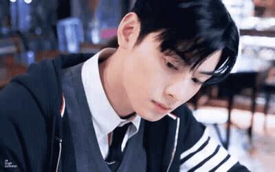 A Young Man In A Suit And Tie Is Sitting At A Table Looking Down . GIF