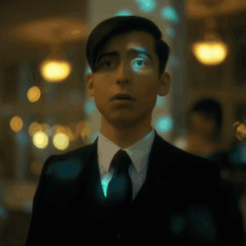 A Young Man In A Suit And Tie Is Standing In A Dark Room . GIF