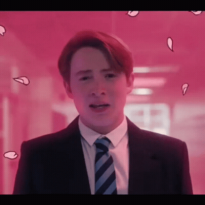 A Young Man In A Suit And Tie Is Standing In Front Of A Pink Wall . GIF