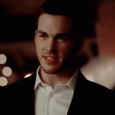 A Young Man In A Suit And White Shirt Is Looking At The Camera . GIF