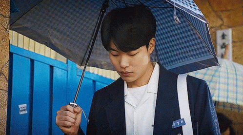 A Young Man In A Suit Is Holding A Blue Umbrella . GIF