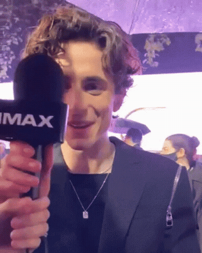 A Young Man In A Suit Is Holding A Microphone In His Hand And Smiling . GIF