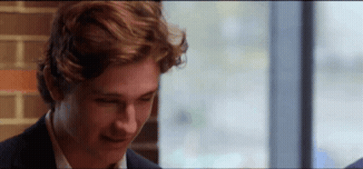 A Young Man In A Suit Is Sitting In Front Of A Window And Smiling . GIF