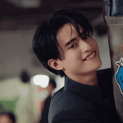 A Young Man In A Suit Is Smiling While Leaning Against A Wall With A Blue Star On It GIF