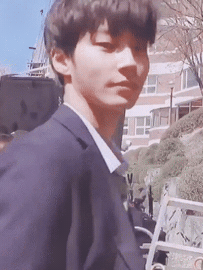 A Young Man In A Suit Is Standing In Front Of A Building Looking At The Camera . GIF