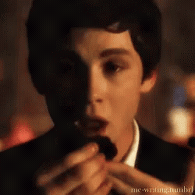 A Young Man In A Tuxedo Is Eating A Chocolate Cookie . GIF