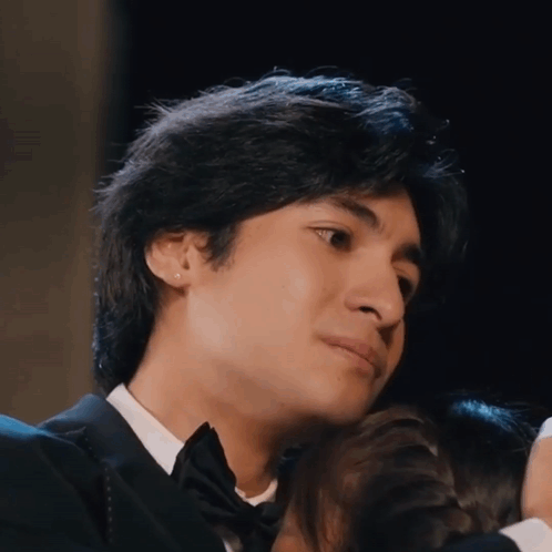 A Young Man In A Tuxedo Is Hugging A Woman GIF