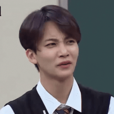 A Young Man In A Vest And Tie Is Making A Funny Face In Front Of A Blackboard . GIF