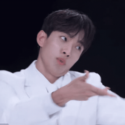 A Young Man In A White Coat Is Making A Funny Face While Pointing At Something . GIF