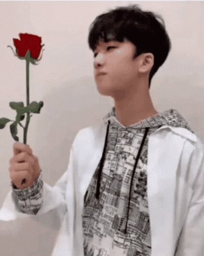 A Young Man In A White Jacket Holds A Red Rose In His Hand GIF