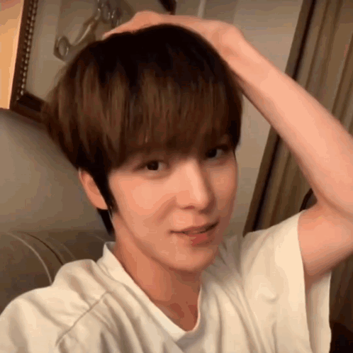 A Young Man In A White Shirt Is Holding His Hair In His Hand . GIF