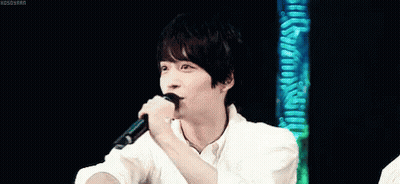 A Young Man In A White Shirt Is Holding His Hand To His Forehead . GIF