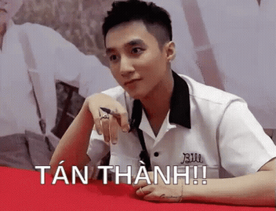 A Young Man In A White Shirt Is Sitting At A Table With His Hand On His Chin . GIF