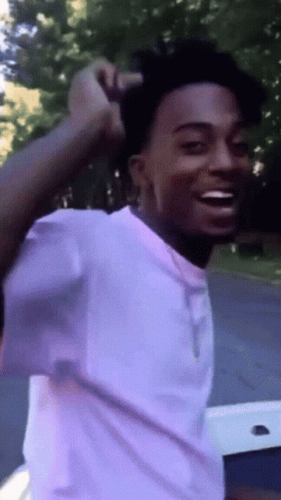 A Young Man In A White Shirt Is Smiling And Holding His Hair GIF
