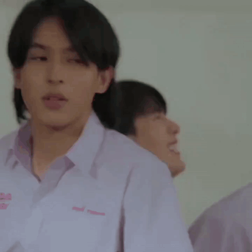 A Young Man In A White Shirt Is Standing In Front Of A Blackboard . GIF