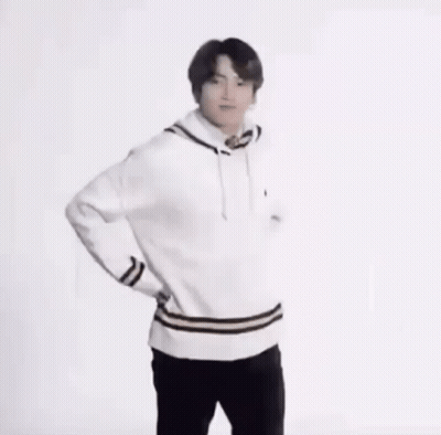 A Young Man In A White Sweater And Black Pants Is Standing With His Hands On His Hips And Smiling . GIF