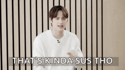 A Young Man In A White Sweater Is Sitting In Front Of A Wooden Wall And Making A Funny Face . GIF