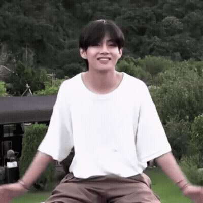 A Young Man In A White T-Shirt And Brown Shorts Is Sitting On A Lawn With His Arms Outstretched . GIF