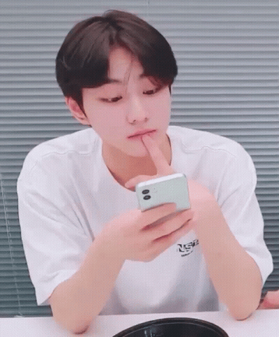 A Young Man In A White T-Shirt Is Looking At A Cell Phone GIF
