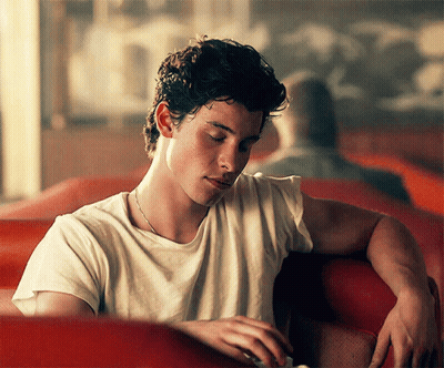 A Young Man In A White T-Shirt Is Sitting In A Red Chair GIF
