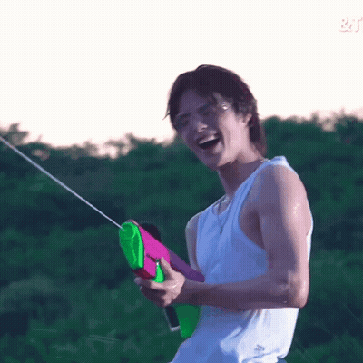 A Young Man In A White Tank Top Is Holding A Water Gun And Laughing . GIF
