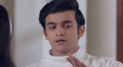 A Young Man In A White Turtleneck Sweater Is Looking At Himself In The Mirror . GIF