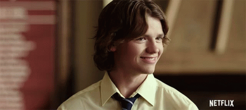 A Young Man In A Yellow Shirt And Tie Is Smiling With A Netflix Logo In The Background GIF