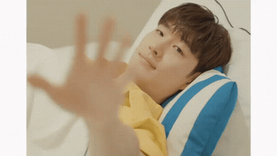 A Young Man In A Yellow Shirt Is Laying In Bed With A Blue And White Striped Pillow GIF