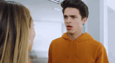 A Young Man In An Orange Hoodie Talks To A Young Woman GIF