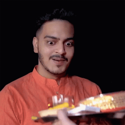 A Young Man In An Orange Shirt Is Holding A Tray Of Food GIF