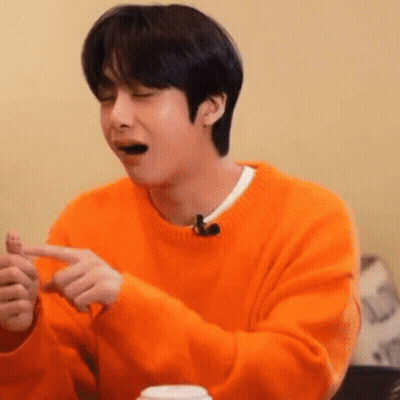 A Young Man In An Orange Sweater Is Sitting At A Table With His Eyes Closed And His Mouth Open . GIF