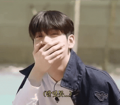 A Young Man Is Covering His Mouth With His Hand And Smiling . GIF