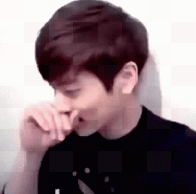 A Young Man Is Covering His Nose With His Hand While Sitting In Front Of A White Wall . GIF