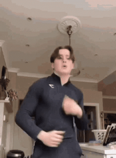 A Young Man Is Dancing In A Living Room While Wearing A Blue Shirt . GIF