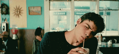 A Young Man Is Drinking A Milkshake Through A Straw In A Restaurant . GIF