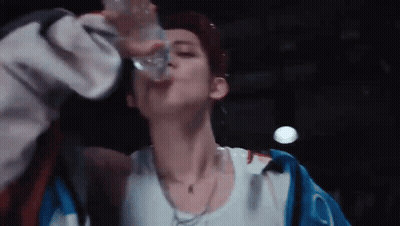 A Young Man Is Drinking Water From A Bottle . GIF