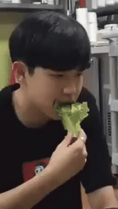 A Young Man Is Eating A Piece Of Lettuce From A Plate . GIF