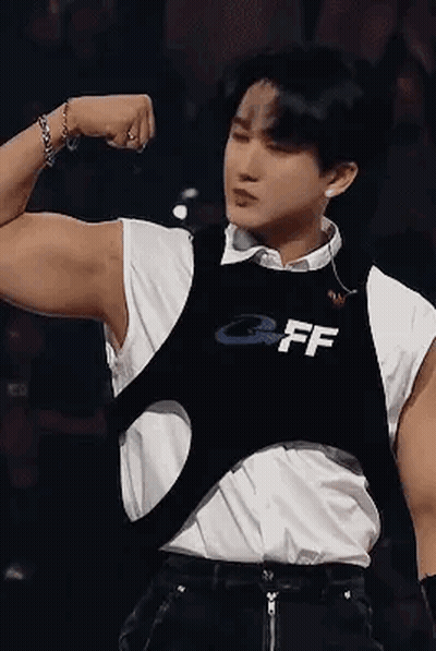 A Young Man Is Flexing His Muscles On A Stage While Wearing A Black Vest . GIF