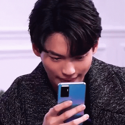 A Young Man Is Holding A Blue Cell Phone In His Hand And Looking At It . GIF