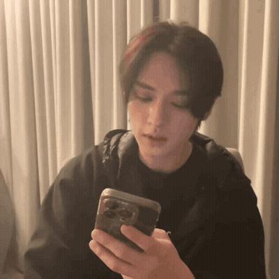 A Young Man Is Holding A Cell Phone In His Hand . GIF